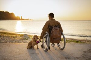 Man in a wheelchar with total temporary disability sitting with his dog looking at sunset